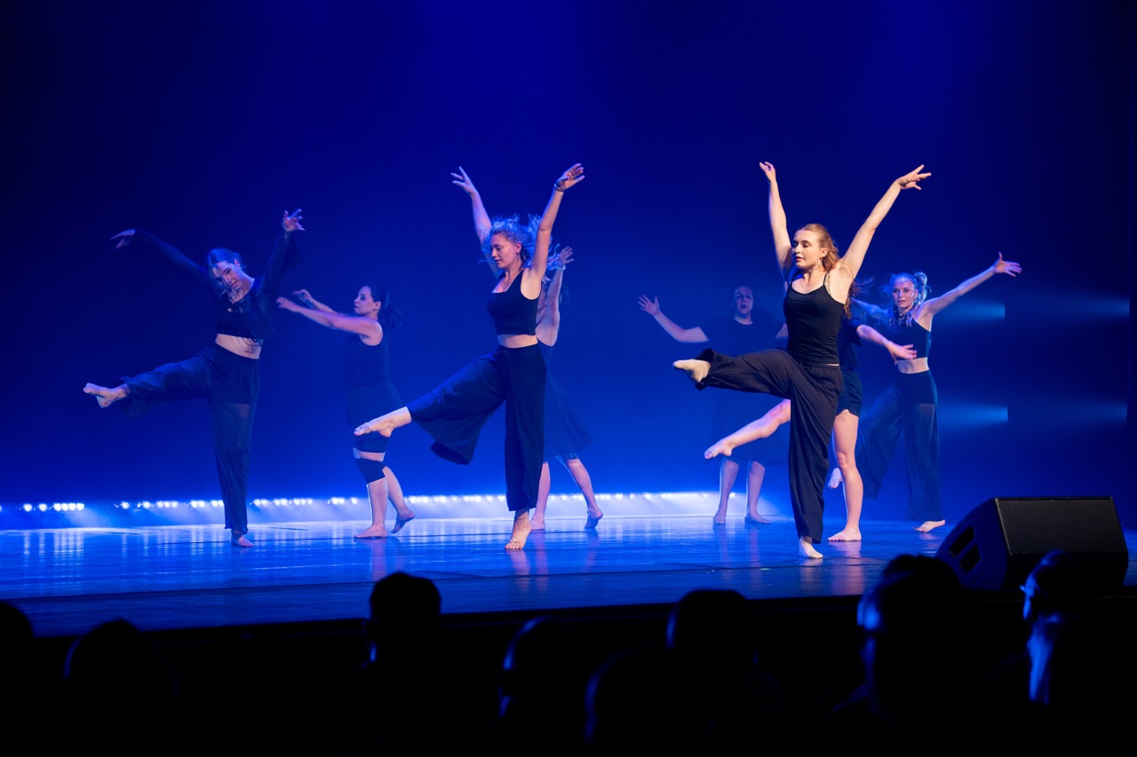 Jazz-Dance-Gruppe von Boom Base mit Sprüngen auf blau beleuchteter Bühne